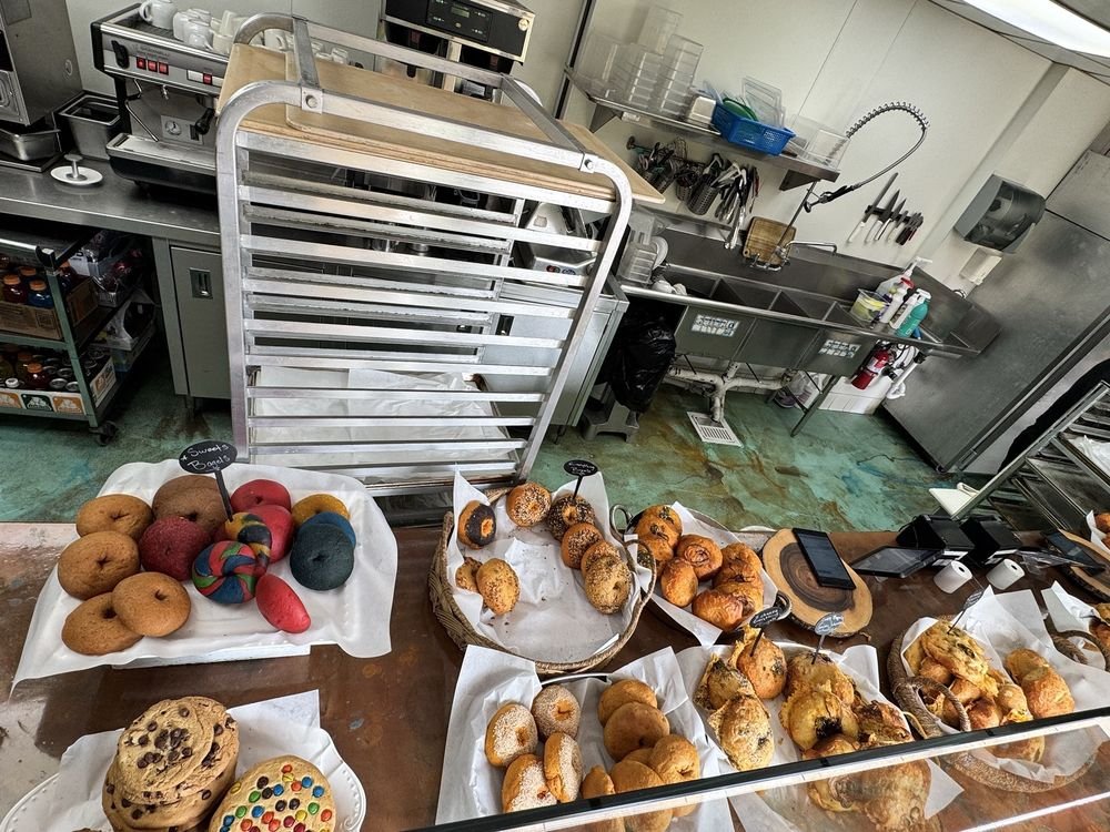 Counter display at Bagelicious Café with rainbow sweet bagels, baskets of bagels and cookies