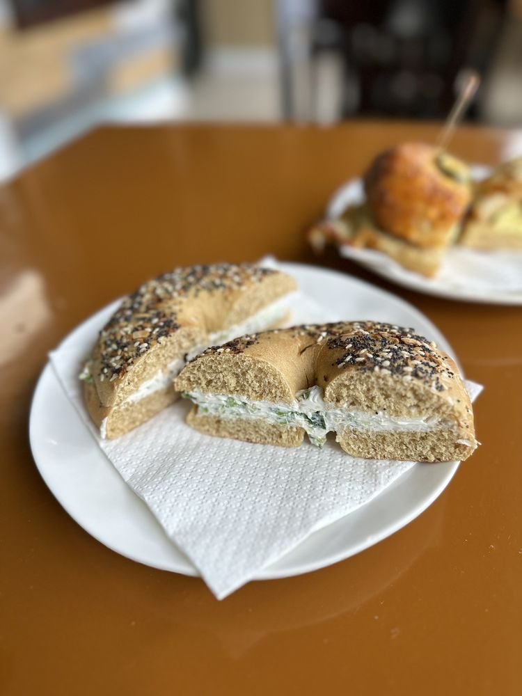 Everything bagel with cream cheese and greens, cut in half on a white plate