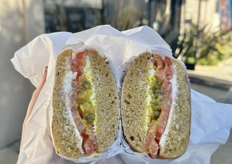 Bagel sandwich with cream cheese and capers held in paper outside