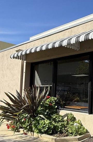 Bagelicious Café front with a striped awning, windows and a planter of geraniums and flax